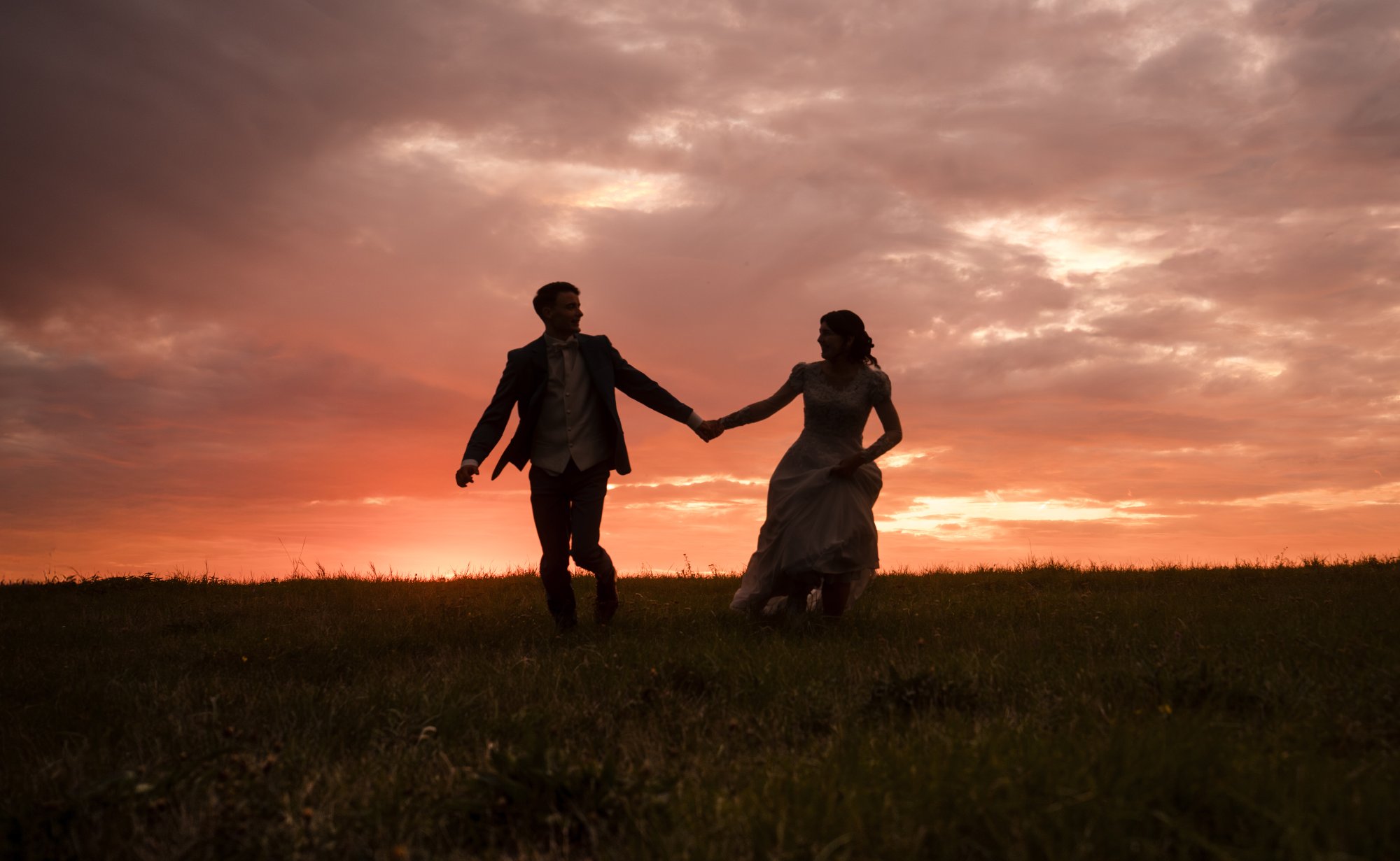 Brautpaar läuft Hand in Hand in den Sonnenuntergang